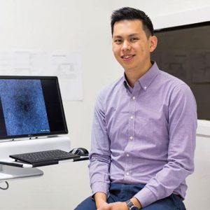 Photo of Dr Zhichao Wu sitting face to camera next to a computer displaying eye imaging in a CERA lab.