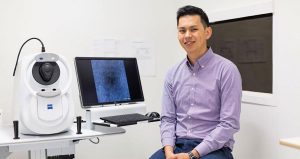 Photo of Dr Zhichao Wu sitting face to camera next to a computer displaying eye imaging in a CERA lab.