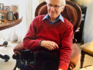 Dr Ian Robertston in a red pullover seated at home with cat