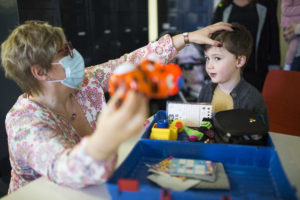 Dr Sandra Staffieri performs an eye test on a little boy. She is wearing a mask and facing him, inspecting his eye, while holding a toy to the side for him to focus on.