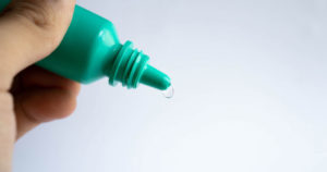 Photograph of a thumb and forefingers holding a green eyedrop bottle.