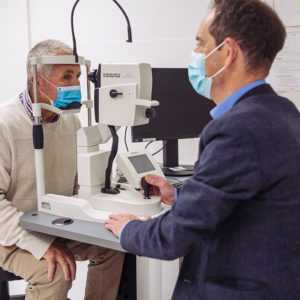 Head and shoulders shot of Professor Keith Martin testing patient Peter Pittman's eyes in the clinic. They are looking toward each other.