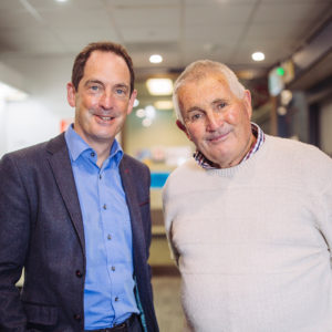 Head and shoulders shot of Professor Keith Martin and patient Peter Pittman. They are standing side by side and smiling in a hallway