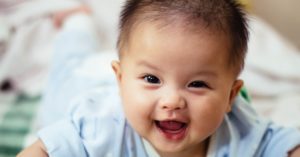 Photograph of baby lying down and smiling to camera.