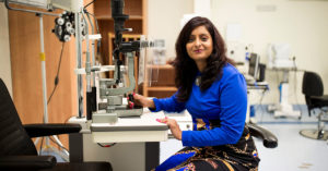 An image of CERA researcher Dr Srujana Sahebjada sitting next to a slit lamp; a common tool used to examine a patient's eye