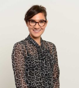 Photograph of Dr Michelle Waugh standing face to camera against a white background, smiling.