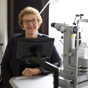 Photo of Professor Robyn Guymer AM sitting behind a slit lamp. She is smiling and facing the camera.