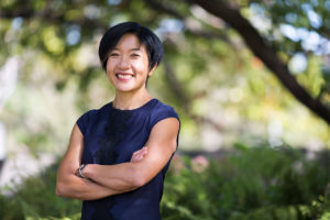 A photo of Associate Professor Lyndell Lim outside. Trees are in the background, she has her arms crossed and is smiling.