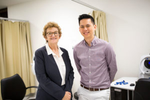A photo of Robyn Guymer and Zhichao Wu standing next to one another in a clinic. Both are smiling and looking directly at the camera
