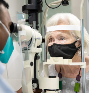 Photograph of research participant Jill being examined by CERA Senior Research Fellow, Associate Professor Sanj Wickremasinghe. Jill is on the right-hand side of the frame, her chin resting on a slit lamp. On the left-hand side, partly cut off, is Associate Professor Wickremasinghe. looking through the lamp.