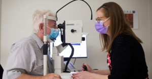 Photograph of Jim being examined by Senior Research Coordinator Lauren Hodgson. Jim is to the left-hand side, his chin resting on a slight light. In the centre is the slit light, and to the right-hand side is Lauren Hodgson looking through the slit light.