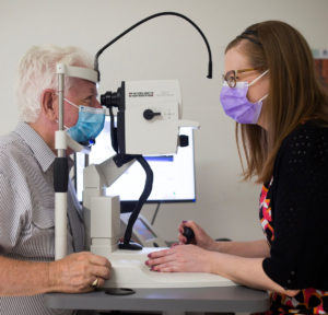 Photograph of Jim being examined by Senior Research Coordinator Lauren Hodgson. Jim is to the left-hand side, his chin resting on a slight light. In the centre is the slit light, and to the right-hand side is Lauren Hodgson looking through the slit light.