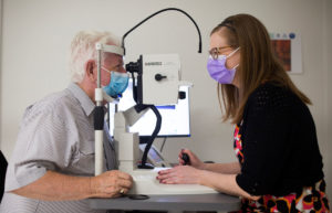 Photograph of Jim being examined by Senior Research Coordinator Lauren Hodgson. Jim is to the left-hand side, his chin resting on a slight light. In the centre is the slit light, and to the right-hand side is Lauren Hodgson looking through the slit light.
