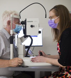Photograph of Jim being examined by Senior Research Coordinator Lauren Hodgson. Jim is to the left-hand side, his chin resting on a slight light. In the centre is the slit light, and to the right-hand side is Lauren Hodgson looking through the slit light.