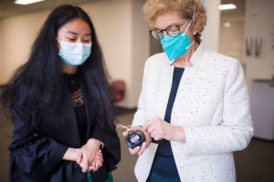 Wendy Fang and Robyn Guymer, standing next to one another in a hallway, examining a pulse oximeter Robyn is holding in her hand.