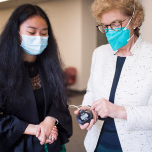 Wendy Fang and Robyn Guymer, standing next to one another in a hallway, examining a pulse oximeter Robyn is holding in her hand.