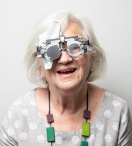 Head and shoulders photograph of research participant Jill against a light grey background. She is wearing a trial lens frame and smiling to camera.