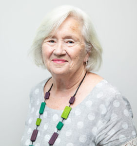 Head and shoulders photograph of research participant Jill, smiling, face to camera. against a light grey background.