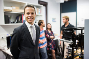 Peter van Wijngaarden, standing next to a camera with several people out of focus in the background
