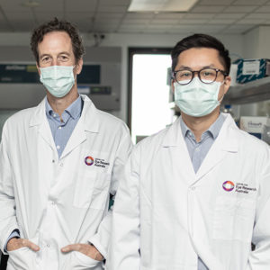 Dr Edwards and Dr Wang, standing next to one another in a lab, wearing face masks and matching lab coats