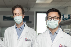 Dr Edwards and Dr Wang, standing next to one another in a lab, wearing face masks and matching lab coats
