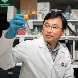 A man standing in a lab examining a test tube
