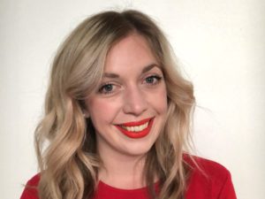A blonde woman, smiling, wearing a red shirt