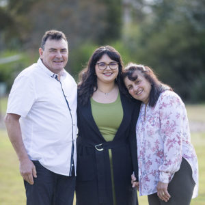 Jasmine standing in between her father and mother outside in an open space