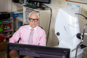 Robert Zent, sitting in front of a monitor and next to an ophthalmic device