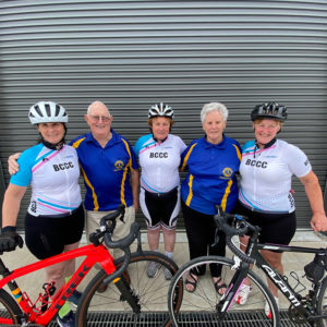 Three sisters in cycling gear, standing with their parents in front of two road bikes.