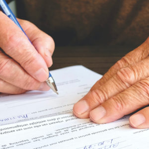 An older person's hands, writing and filling out a form