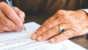 An older person's hands, writing and filling out a form