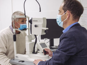 Head and shoulders shot of Professor Keith Martin testing patient Peter Pittman's eyes in the clinic. They are looking toward each other.