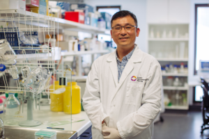 Assoicate Professor Associate Professor Guei-Sheung (Rick) Liu standing in a lab with equipment behind him.