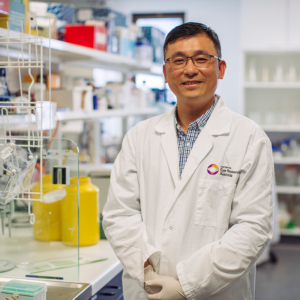 Assoicate Professor Associate Professor Guei-Sheung (Rick) Liu standing in a lab with equipment behind him.