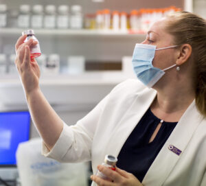 Image of Heather Machin wearing a mask and looking at a vial she's holding in the lab