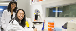 Dr Jennifer Fan Gaskin & Dr Elsa Chan in the lab and smiling toward the camera.